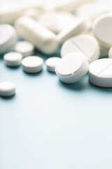 Various white pills on blue background against backlight.