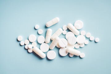 Various white pills on blue background against backlight.