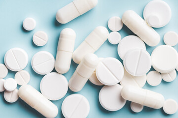 Various white pills on blue background against backlight.