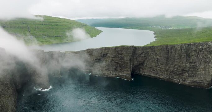 Aerial view of Sorvagsvatn lake with its steep cliffs plunging into the ocean, shrouded in mist, contrasting with the green hills, Sorvagsvatn lake, Faroes.