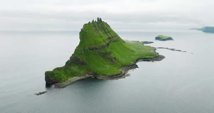 Aerial view of the verdant Tindholmur islet rising majestically from the sea, its steep cliffs contrasting with the calm waters, Tindholmur, Faroes.