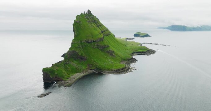 Aerial view of the majestic Tindholmur islet, its steep green cliffs rising boldly from the sea, a stark contrast to the tranquil water, Tindholmur, Faroes.