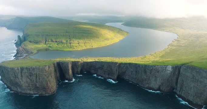 Aerial view of the tranquil Sorvagsvatn lake contrasting with rugged cliffs, where green meadows meet the deep blue sea, Sorvagsvatn lake, Faroes.