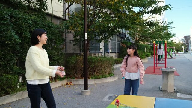Adorable japanese girl playing otedama with her mother in an urban playground in Japan