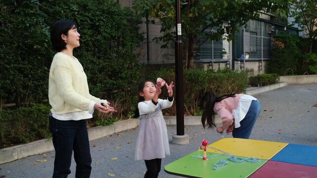Happy Asian mother playing otedama with her two young daughters in a park in Japan