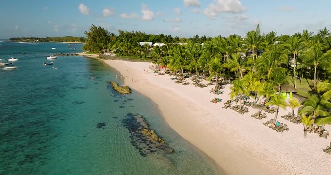 Aerial view of the turquoise water gently lapping against the white sands dotted with palm trees and sunbeds, Grand Baie, Mauritius.