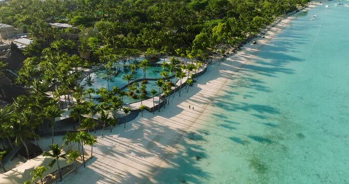 Aerial view of the turquoise ocean caressing the white sandy beach, fringed by swaying palms and lush greenery, Grand Baie, Mauritius.