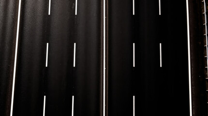 Pristine black asphalt highway with sharp white dividing lines, captured from a top-down aerial perspective, symbolizing journey and clarity.