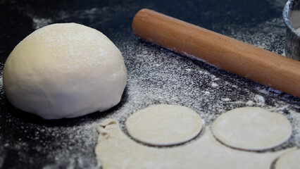 Rolled dough circles, rolling pin, flour sieve and fresh dough ball on dark kitchen background. Traditional cooking concept, rustic food preparation, homemade cuisine.