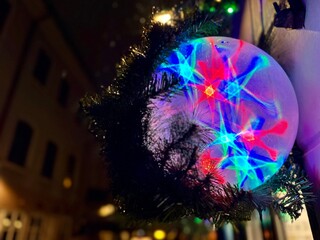 Colorful glowing spherical ball decoration against a city street with lights and bokeh. Festive atmosphere in the night urban environment. Christmas greeting card with copy space