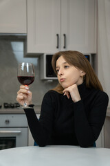 Young woman savoring a glass of red wine in a stylish modern kitchen, reflecting on the moment with a thoughtful expression while enjoying a peaceful break indoors