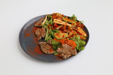 Salad with grilled veal and vegetables on a dark plate on a white background, restaurant serving