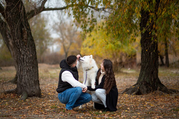 A young family - a guy, a girl and a cute fluffy Samoyed - are walking by the river