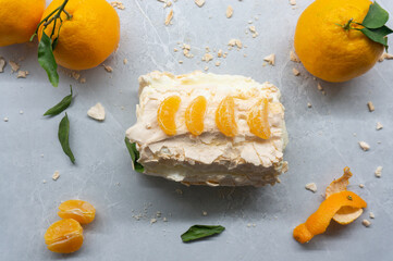 A delicious meringue roll with fruit. A top view of the meringue cake and tangerines against a gray background.