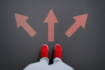 Choice concept with red arrows and sneakers on asphalt background