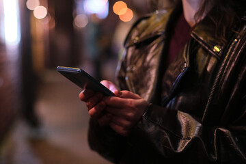 Woman using mobile phone outdoors on city street at night 