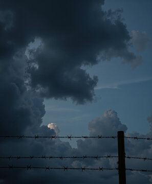 Barbed wire fence under dramatic dark clouds at twilight, Day of Remembrance for the Victims of Genocide in World War II  