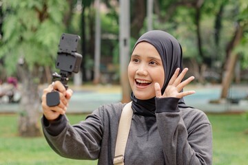 A young Indonesian Muslim woman making a vlog video using an action camera in a city park