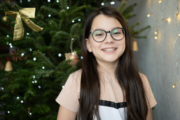 Teenage girl smiling brightly with visible teeth near decorated Christmas tree, joyful holiday childhood emotion and dental concept