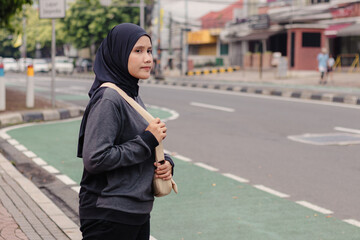 A young Indonesian Muslim woman standing on the side of the road to cross the road or waiting for a taxi