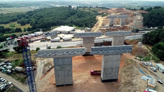 Drone aerial view of a large highway viaduct construction site with reinforced concrete bridge piers and superstructure elements. Major infrastructure and civil engineering project in progress.