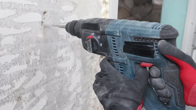Close-up view of construction worker drilling concrete wall using electric power drill. Renovation and repair process, wall preparation for electrical installation, cable mounting and building interio