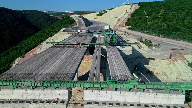 Drone aerial view of highway viaduct deck construction with steel girders and concrete piers. Large-scale infrastructure and civil engineering project in mountainous terrain.