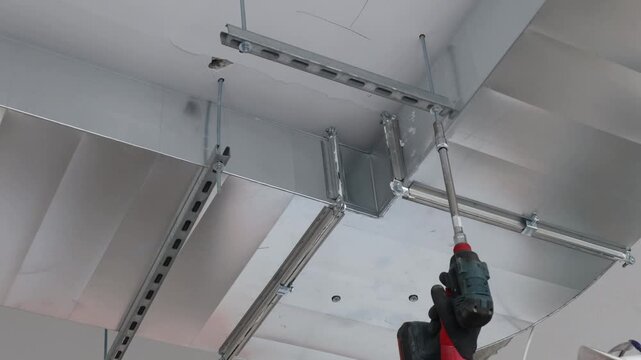 Close-up of construction worker installing metal ceiling frame using cordless drill. Professional drywall ceiling installation, interior renovation process, suspended ceiling system, building construc