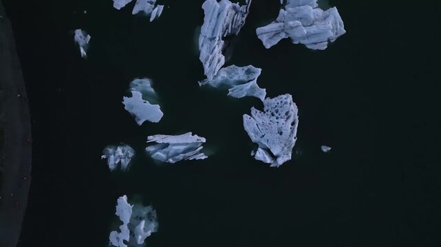 Golden hour aerial flight reflecting warm sunset light on blue ice chunks at J&ouml;kuls&aacute;rl&oacute;n lagoon, Iceland.