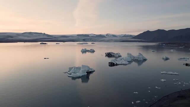 Golden hour aerial flight reflecting warm sunset light on blue ice chunks at J&ouml;kuls&aacute;rl&oacute;n lagoon, Iceland.