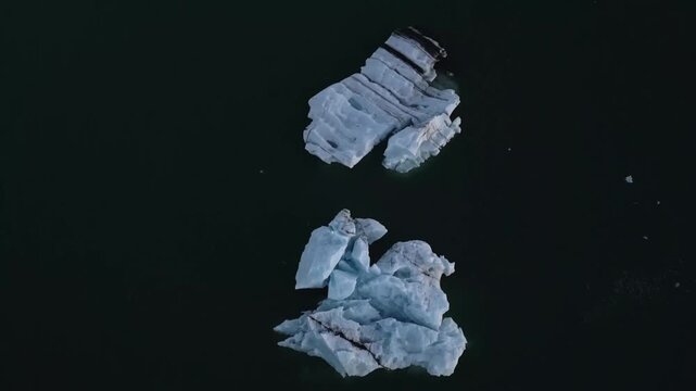 Golden hour aerial flight reflecting warm sunset light on blue ice chunks at J&ouml;kuls&aacute;rl&oacute;n lagoon, Iceland.