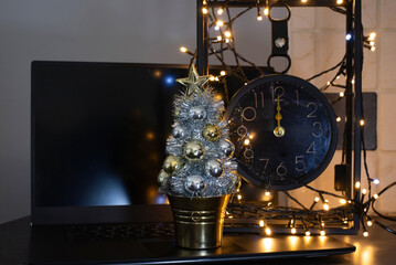 A festive desk setup features a small silver Christmas tree, a large black clock, and warm fairy lights arranged around laptop. Time to celebrate, not work
