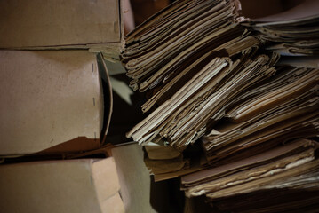 Weathered stacks of old newspapers and cardboard boxes in a storage area, creating sense of history, clutter, and forgotten documents awaiting organization. Old accounting documents