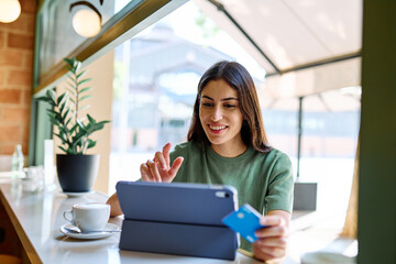 Young woman using credit card for online shopping on her tablet computer drinking coffee in caffee cafeteria