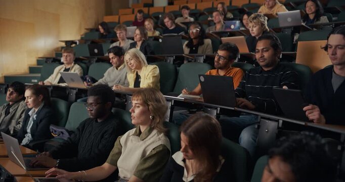 Diverse Group of College Students Concentrate in Lecture Hall, Typing on Laptops, writing Notes, Listening During University Course on Modern Academic Learning, Research, and Professional Development.