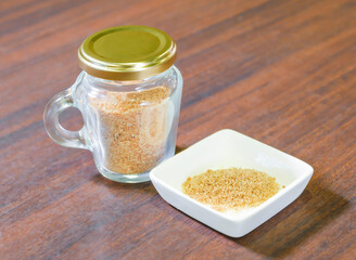 Brown sugar in glass jar with gold lid and small white bowl on wood