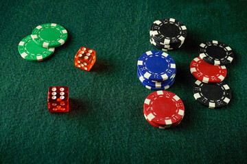Red, green, blue, and black poker chips are neatly stacked alongside two brightly colored dice with winning numbers on a green felt table. Friends gather for a fun evening