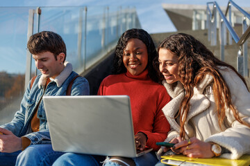Diverse group of college students smiling and studying together on laptop outdoors