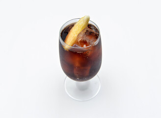 Refreshing dark soda with ice and a citrus wedge served in an elegant stemmed glass against white