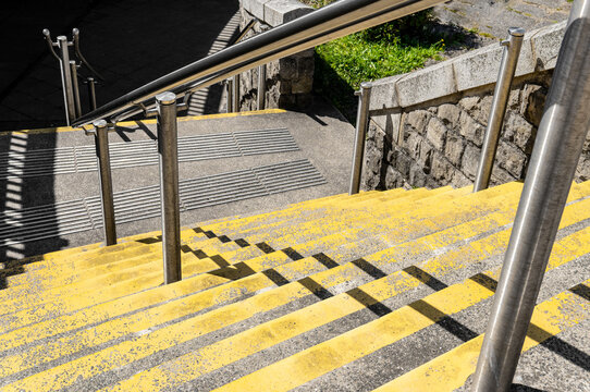Yellow concrete stairs with metallic banister to hold on for safety in an urban environment. It is leading to a city park.