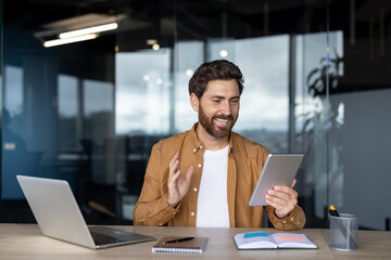 Man smiling during an online video call using a digital tablet at his office desk, actively communicating and participating in a remote virtual meeting