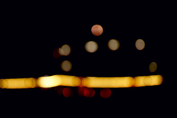 Defocused city lights forming blurred circular and horizontal shapes on dark background. Warm