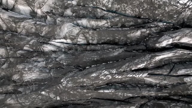 Cinematic aerial drone view of Sv&iacute;nafellsj&ouml;kull glacier tongue showing dramatic blue ice and volcanic ash textures in Iceland 4K.