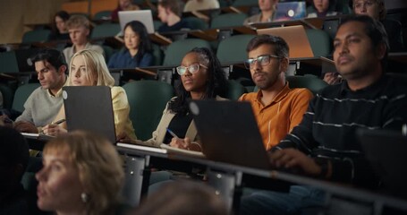 University Students Sit in Lecture Hall, Typing on Laptops, Writing Notes, and Exchanging Ideas While Concentrating on Presentation, Study, Academic Collaboration, and Modern Digital Learning Tools. - Powered by Adobe