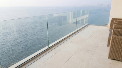 Fototapeta premium Modern seaside balcony with glass railing overlooking calm ocean and hazy horizon under soft daylight atmosphere