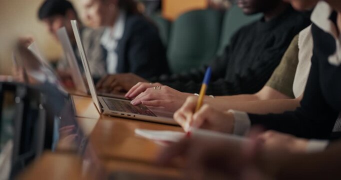 University Students Sit in a Lecture Hall Row, Typing on Laptops and Writing Notes, Concentrating on Coursework, Digital Research, Academic Learning During Class Session and Organized Study Habits.