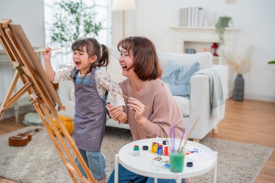 Mom and daughter spend time painting together in a bright living room on a weekend afternoon