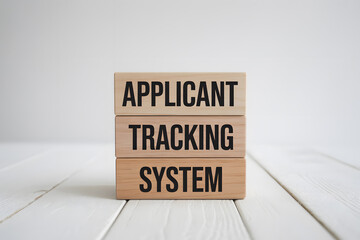 Minimalist image of three stacked wooden blocks displaying APPLICANT, TRACKING, and SYSTEM in bold black text on a light wooden surface, evoking a modern, professional atmosphere.