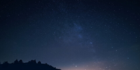 Fototapeta premium Night sky filled with stars over a forest at dusk