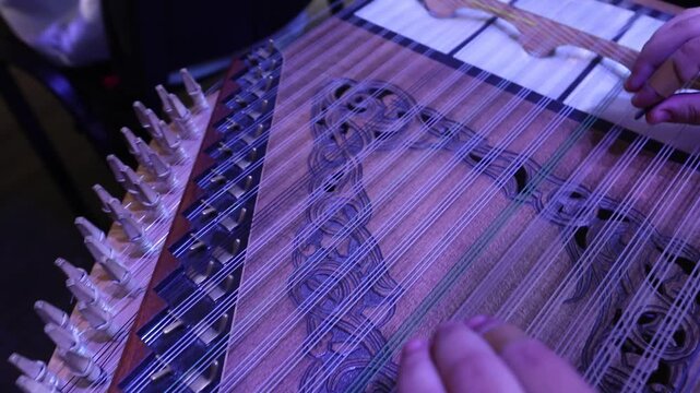 Close-up of musician's hands playing the Qanun. The artist plucks strings and adjusts tuning levers on this traditional Middle Eastern string instrument during a live musical concert performance.

